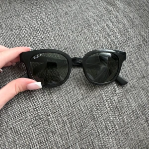 Ray-Ban solglasögon - Snygga svarta solglasögon från Ray-Ban med klassisk rundad form och polariserade mörka glas. Tjock båge i plast med Ray-Ban-logga på sidan. Perfekta för att ge din look en cool vibe och skydda ögonen mot solen.