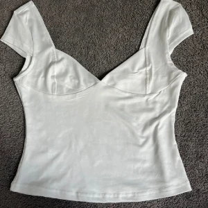 Vit v-ringad topp med kort ärm - Snygg vit topp med v-ringning och korta ärmar. Figurnära passform och lätt stretchigt material som känns mjukt mot huden. Perfekt att styla med jeans eller kjol för en clean look.