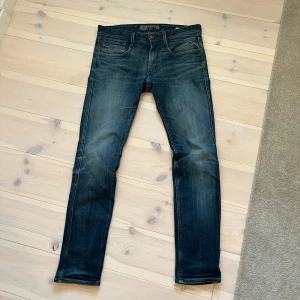 Replay Anbass jeans i mörkblå denim - Snygga Replay Anbass jeans i mörkblå tvätt med slitningar och klassiska fem fickor. Jeansen har smal passform, låg midja och detaljerade bakfickor med Replay-logga. Tillverkade i stretchig bomullsdenim för extra komfort.