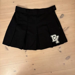 Svart plisserad kortkjol med patch - Snygg svart plisserad kortkjol med bred linning. Knappt använd. 