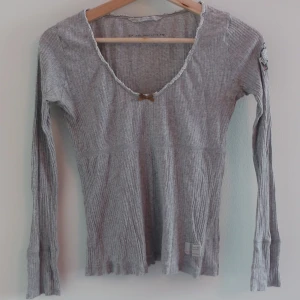 Grå ribbad topp från Odd Molly - Supersöt grå ribbad topp från Odd Molly med lång ärm och en liten rosett framtill. Passar bra till jeans eller kjol.
