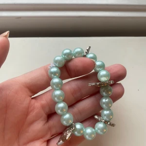 Turkost pärlarmband med silverfärgade berlocker - Stretchigt armband med stora turkosa pärlor och fyra silverfärgade berlocker i form av löv. Pärlorna har en glansig finish och armbandet ger en lekfull och trendig vibe. Perfekt för att addera lite färg och personlighet till din look. Egengjord 