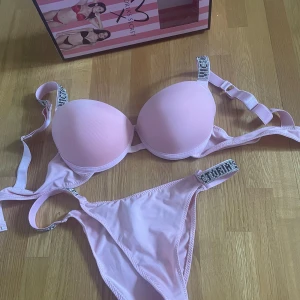 Rosa underkläder sätt från Victoria's Secret - Supersöt ljusrosa underkläder från Victoria's Secret med vadderad bygel-bh och matchande trosa. Axelbanden har glittriga detaljer med text och ger en extra lyxig känsla. Låda följer med är helt ny inte ens provat fick i present. Bh är stl 85b och trosorna passar s/m dom är stretchiga.