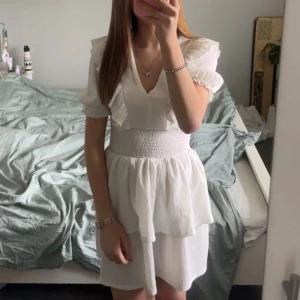 Vit volangklänning med puffärm - Supersöt vit kortklänning från Gina tricot med v-ringning, volangdetaljer och puffärmar. Smockad midja klänningen är i storlek xs men passar mig som har xxs vanligtvis. Pris går att diskuteras ! (FÖRRA ÄGARENS BILD) 