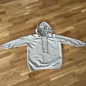 Beige hoodie med snörning - En stilren beige kashmir hoodie med huva och snörning. Tröjan har lång ärm och är tillverkad i mjukt material som känns skönt mot huden. Perfekt för en avslappnad look och enkel att matcha med jeans eller joggers.