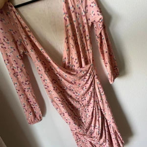 Blommig rosa omlottklänning - Supersöt rosa omlottklänning med små blommor i lila, blått och vitt. Klänningen har lång ärm, djup v-ringning och snygg drapering i midjan. Perfekt för dig som gillar romantisk och chill stil.
