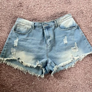 Blå jeansshorts med fransar från SHEIN - Snygga blå jeansshorts från SHEIN Curve med slitna detaljer och fransig kant. Modellen är högmidjad och har både fram- och bakfickor. Perfekta för sommaren när du vill ha en chill och trendig look.