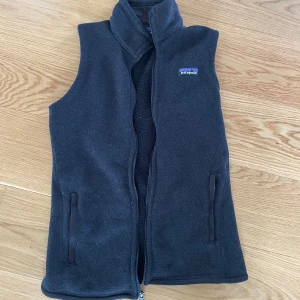 Svart fleeceväst från Patagonia - Svart fleeceväst från Patagonia med hög krage och hel dragkedja framtill. Västen har två fickor med dragkedja och en liten broderad Patagonia-logga på bröstet. Perfekt till sommaren och våren. Står S men passar xs bättre. 