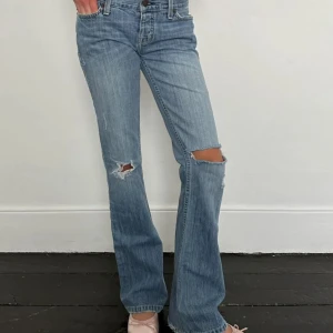 Blå bootcut jeans från Hollister - Snygga ljusblå bootcut jeans från Hollister med slitna detaljer och hål på knäna. Klassisk femficksmodell med broderade bakfickor och läderpatch i midjan. Perfekta för en avslappnad och trendig look.