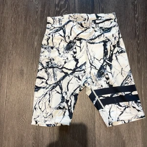 Svartvita mönstrade cykelshorts - Snygga cykelshorts med svartvitt marmormönster och två svarta ränder på ena benet. De är stretchiga och sitter tajt, perfekta för träning eller en sportig look. Hög midja och tillverkade i ett mjukt, syntetiskt material som andas.