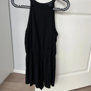Svart jumpsuit - Snygg svart jumpsuit från Atmosphere med smala axelband och markerad midja. Ärmlös och har en enkel, stilren design som passar perfekt till många tillfällen. Öppning baktill. Lätt och luftig, perfekt för varmare dagar. Skulle nog säga att den är liten i storlek. 