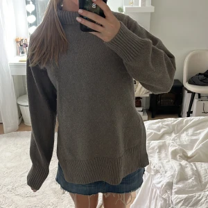Grå stickad polotröja med slits - Mysig grå stickad polotröja med ribbade muddar och hög krage. Tröjan har en loose passform och slits i sidorna för extra chill vibe. Perfekt att slänga på sig över jeans eller kjol när det är kallt ute.