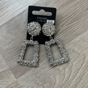 Örhängen från Montini - Statementörhängen i silverfärg från Montini. Örhängena har en rund topp och en rektangulär hängande del. Perfekta för att sticka ut och ge din look extra edge. Cirka 7 centimeter och helt oanvända. 
