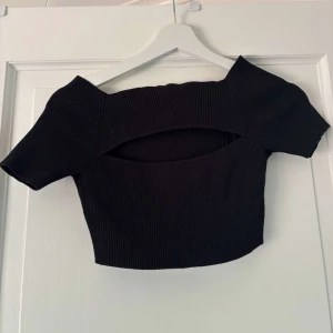 Svart ribbad croppad topp Pull&Bear - Svart ribbad croppad topp från Pull&Bear med korta ärmar och en snygg cut-out detalj framtill. Toppen har en tight passform och är perfekt för dig som gillar trendiga och stilrena plagg. Materialet är stretchigt och bekvämt.