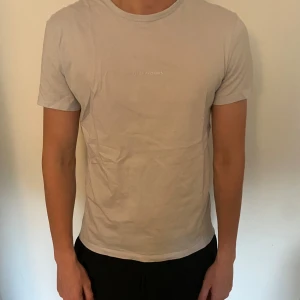 Beige t-shirt från L'Atelier Archives - Snygg beige t-shirt från L'Atelier Archives Paris med minimalistisk logga på bröstet. Inte kommit till användning så är i bra skick!
