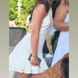 Vit kort klänning med volang - Superfin vit kort klänning från Zara med volangkant nertill och öppen rygg med snygga banddetaljer. Klänningen har halterneck och är ärmlös, perfekt för student eller sommarens alla tillfällen. Använd 1 gång till studenten. Nypris 600