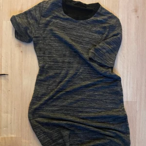 Mörkgrå melerad t-shirt - En mörkgrå melerad t-shirt med korta ärmar och rund halsringning. T-shirten har en enkel och stilren look med svart kant vid halsen. Perfekt för en chill och avslappnad stil.