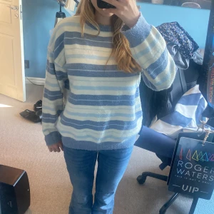 Randig blå och vit stickad tröja - Mysig stickad tröja med breda ränder i blått och vitt. Tröjan har en relaxed fit, rund halsringning och långa ärmar. Perfekt för kyliga dagar och enkel att styla med jeans eller kjol.