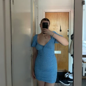 Blå prickig kort klänning från Zara - Supersöt blå kort klänning från Zara med vita prickar, puffiga korta ärmar och knytning framtill på bröstet. Figurnära passform och lätt rynkade detaljer längs sidorna. Dragkedja i sidan. 