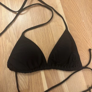 Svart trekantsbikini med knytband - En stilren svart trekantsbikini med tunna knytband i sidorna och runt nacken. Bikinin har en klassisk form med justerbara band och lätt vaddering på insidan. Perfekt för stranden eller poolen och enkel att matcha med andra plagg. Säljer en likadan i vit, köper man båda för man de för ett billigare pris! 