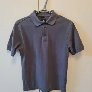 Grå pikétröja från Active Wear strl S - Säljer en grå pikétröja från Active Wear i storlek S. Tröjan har klassisk krage, tre knappar framtill och korta ärmar. Underarmen har ventilationshål (se bild). Kan hämtas i Vallentuna.