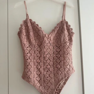 Puderrosa virkad body med blommönster - Supersöt puderrosa body från H&M med tunna axelband och v-ringning. Hela toppen är täckt av virkade blommor i spets och har en romantisk vibe. Perfekt för varma dagar eller när du vill känna dig extra fin