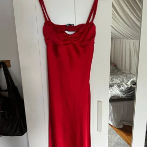 Röd långklänning från Zara i satin - Supersnygg röd långklänning från Zara i glansigt satinmaterial. Klänningen har smala axelband, öppen rygg och en liten rynkdetalj vid bysten. Perfekt för dig som vill sticka ut och känna dig extra glam.