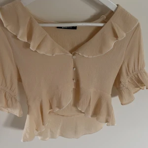 Beige blus med volang från Gina Tricot - Supersöt beige/gul blus från Gina Tricot.