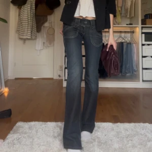 Gråa lågmidjade bootcut jeans - Säljer dessa sjukt coola bootcut jeansen! Uppklippt slits på båda benen. Midja: 38 cm. Innerbenslängd: 86 cm. Bootcut: 19 cm + slits.