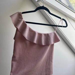 Rosa omlottopp från Stradivarius - Supersöt ljusrosa topp från Stradivarius med en axelbandslös design och volangdetalj längs halsringningen. Denna köptes i Spanien för 350 kr! Skriv privat för yttligare frågor!! Använd 2 ggr❤️ 