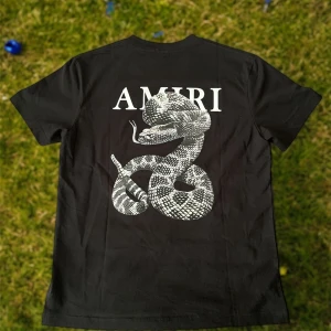 Svart Amiri t-shirt med ormmotiv - Svart t-shirt från Amiri i 100% bomull med stor vit orm-grafik och Amiri-logga på ryggen samt mindre ormmotiv framtill. Klassisk passform och rund halsringning. Perfekt för dig som gillar streetwear med edge.