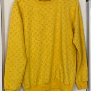 Gul Louis Vuitton sweatshirt - Gul sweatshirt från Louis Vuitton med ikoniskt monogrammönster över hela tröjan. Tröjan har rund hals, ribbade muddar och nederkant. Perfekt statement piece för dig som vill sticka ut med lyxig streetstyle.