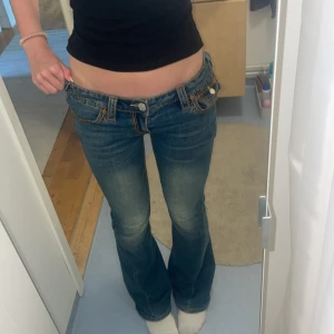 True Religion bootcut jeans låg midja - Säljer ett par blå bootcut jeans från True Religion med låg midja. Jeansen har snygga kontrastsömmar, ikoniska bakfickor med lock och silverfärgade knappar. Materialet är klassisk jeansbomull med lätt slitning framtill för en cool look. Orginalpris 1900 kr 