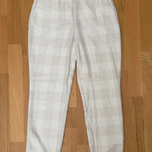 Beige rutiga kostymbyxor H&M 36 - Snygga beige kostymbyxor från H&M i storlek 36. Byxorna har ett rutigt mönster i ljusa toner, raka ben och sidfickor. Perfekta för en clean och stilren look. Materialet känns mjukt och har lite struktur.