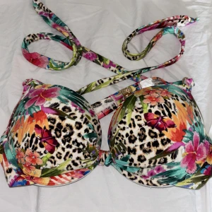 Färgglad bikiniöverdel med leopard och blommor - Snygg bikiniöverdel med leopardmönster och färgglada blommor i rosa, orange och grönt. Bikinin har vadderade kupor och knytband i nacken. storleken är 75A men skulle säga att den är större i storlek och även passar B kupa🩷säljer då jag växt ur den.