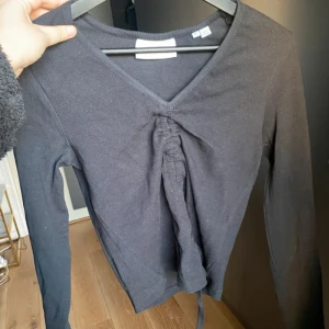 Svart långärmad topp från JJXX - Svart långärmad topp från JJXX med v-ringning och snygg snörningsdetalj framtill. Modellen är ribbad och har en croppad passform som ger en trendig look. Perfekt att matcha med jeans eller kjol för en stilren outfit.