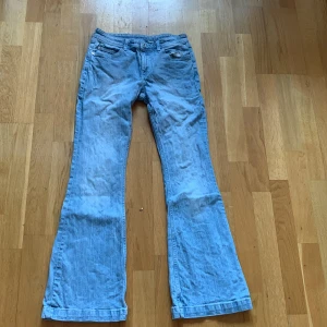 Ljusblå bootcut jeans från H&M - Säljer ett par ljusblå jeans från H&M med bootcut och midja som går att justera. Byxorna har klassisk femficksdesign, knappar på bakfickorna och är i mjukt bomullsmaterial. Perfekta för dig som gillar retrovibbar och bekväm passform.