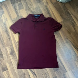 pikétröja Polo Ralph Lauren - Snygg vinröd pikétröja från Polo Ralph Lauren med klassisk krage, korta ärmar och broderad logga på bröstet. Slim fit-modell i stretchig bomull som sitter riktigt schysst. Perfekt för dig som gillar stilrena och tidlösa plagg.