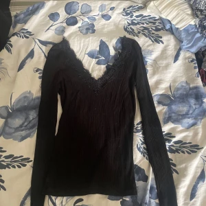 Svart ribbad topp med spets från Amisu - Svart långärmad topp från Amisu i ribbat material med djup v-ringning och snygga spetsdetaljer längs halsen. Har en tajt passfom. Använd ett antal gånger men inget synligt 💞💞