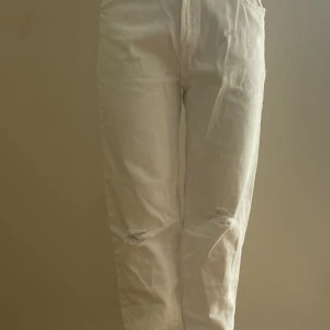 Vita jeans med slitningar från Zara - Snygga vita jeans från Zara i storlek 164. Modellen har raka ben, hög midja och coola slitningar på knäna för en trendig look. Tillverkade i bomull med klassiska bakfickor och dragkedja framtill.