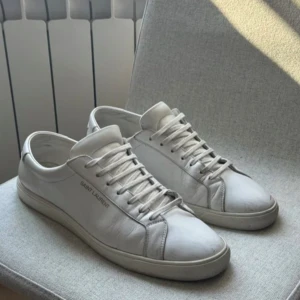 Saint Laurent skor - Snygga vita och unika sneakers från Saint Laurent, klassisk låg modell med platt sula. Diskret logga på sidan och bak på hälen. Stilrena och minimalistiska med vita snören och detaljer. Tillverkade i Italien. Priser är diskuterbart, billigare vid snabba affärer.
