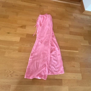 Rosa vida linnebyxor med dragsko - Säljer ett par lrosa linnebyxor med breda ben och avslappnad passform. Byxorna har elastisk midja med snörning och är tillverkade i ett svalt linnematerial. Perfekta för varma dagar när du vill ha något luftigt och bekvämt. Längden på linnebyxorna är kortade och är nu 90 cm från midjan.