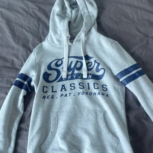 Superdry hoodie - Säljer en riktigt fet grå superdry hoodie. Hoddien bär storleken xs. Trendig och höjer din outfit. Säljer på grund av att den är för liten. Vid frågor och funderingar är de bara att skriva