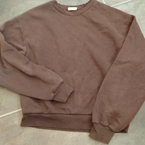 Brun sweatshirt i bomull - Enkel brun sweatshirt med rund hals och ribbade muddar vid ärmslut och nederkant. Tröjan är i mjuk bomull och har en avslappnad passform, perfekt för chill dagar eller när du vill ha en basic look.