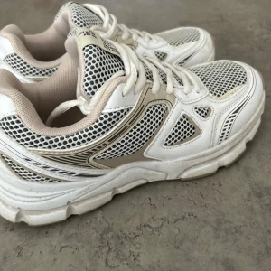 Vita chunky sneakers med meshdetaljer - Snygga chunky sneakers i vitt med beige och svarta meshdetaljer. Skorna har en sportig vibe med tjock sula, snörning och ventilerande meshpaneler. Perfekta för dig som gillar streetstyle och vill ha bekväma skor till vardags.