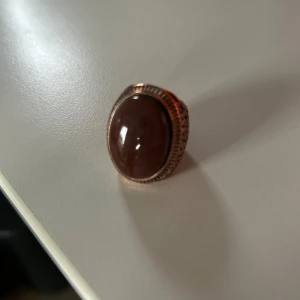 Vintageinspirerad brun statementring - Cool ring med stor oval brun sten och detaljerat guldigt band med mönstrad yta. Ringen har en riktigt retro vibe och sticker ut med sin unika design. Perfekt för dig som gillar att maxa din stil med accessoarer som syns.