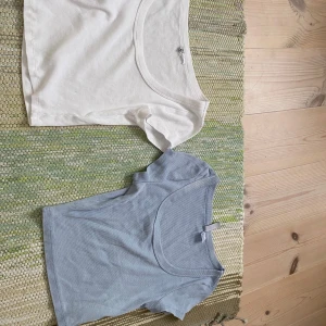 2-pack ribbade croppade toppar H&M S - Säljer två croppade ribbade toppar från H&M Divided i storlek S och xs. En är vit och en är ljusblå, båda med kort ärm och rundad, djup urringning. Perfekta för sommaren och lätta att matcha med jeans eller kjol. Den blå har en fläck vid urringningen. Säljer båda för 60 eller 40 var