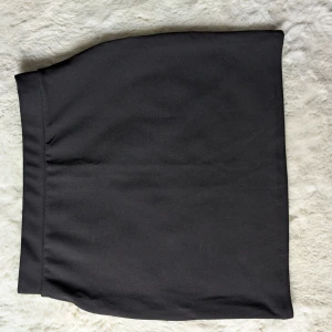 Svart enkel kortkjol - Stilren svart kortkjol med rak passform och bred linning. Perfekt att matcha med en cool t-shirt eller stickad tröja. Kjolen är helfärgad utan detaljer och har en klassisk look som funkar till många olika stilar.