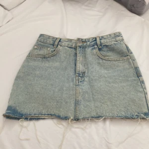 Ljusblå jeanskjol från Pull&Bear - Ljusblå jeanskjol från Pull&Bear som är lite sliten på slutet som gör hela kjolen perfekt. Perfekt för en avslappnad look och nu inför sommaren. Priset kan diskuteras och fråga gärna om fler bilder!!