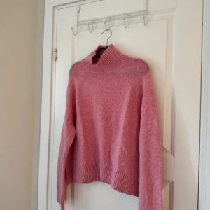 Rosa stickad polotröja - Mysig rosa stickad polotröja med bred ribbad krage och muddar. Tröjan har en loose passform och långa ärmar, perfekt för kyliga dagar. Enkel och stilren design som är lätt att matcha med jeans eller kjol.lite nopprig 